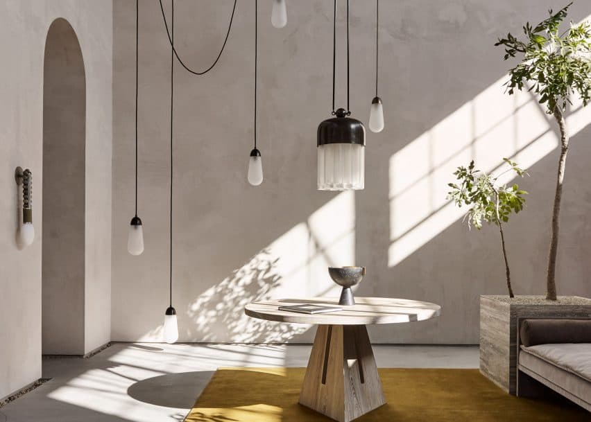 Sun raking across sand-finish walls of Meoded Tonachino Firenze, behind a round table and hanging pendants