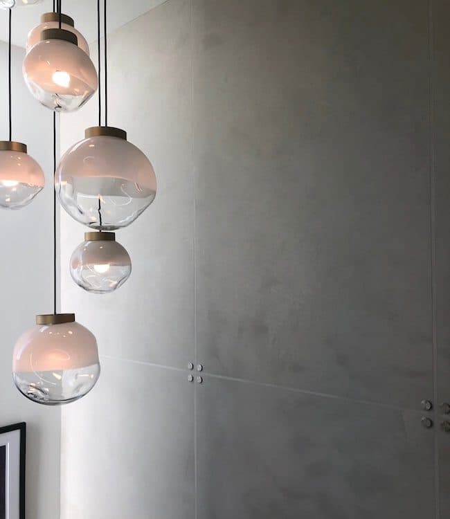 A smooth gray wall of Meoded Golmex concrete-look plaster behind a cluster of glass pendant lights