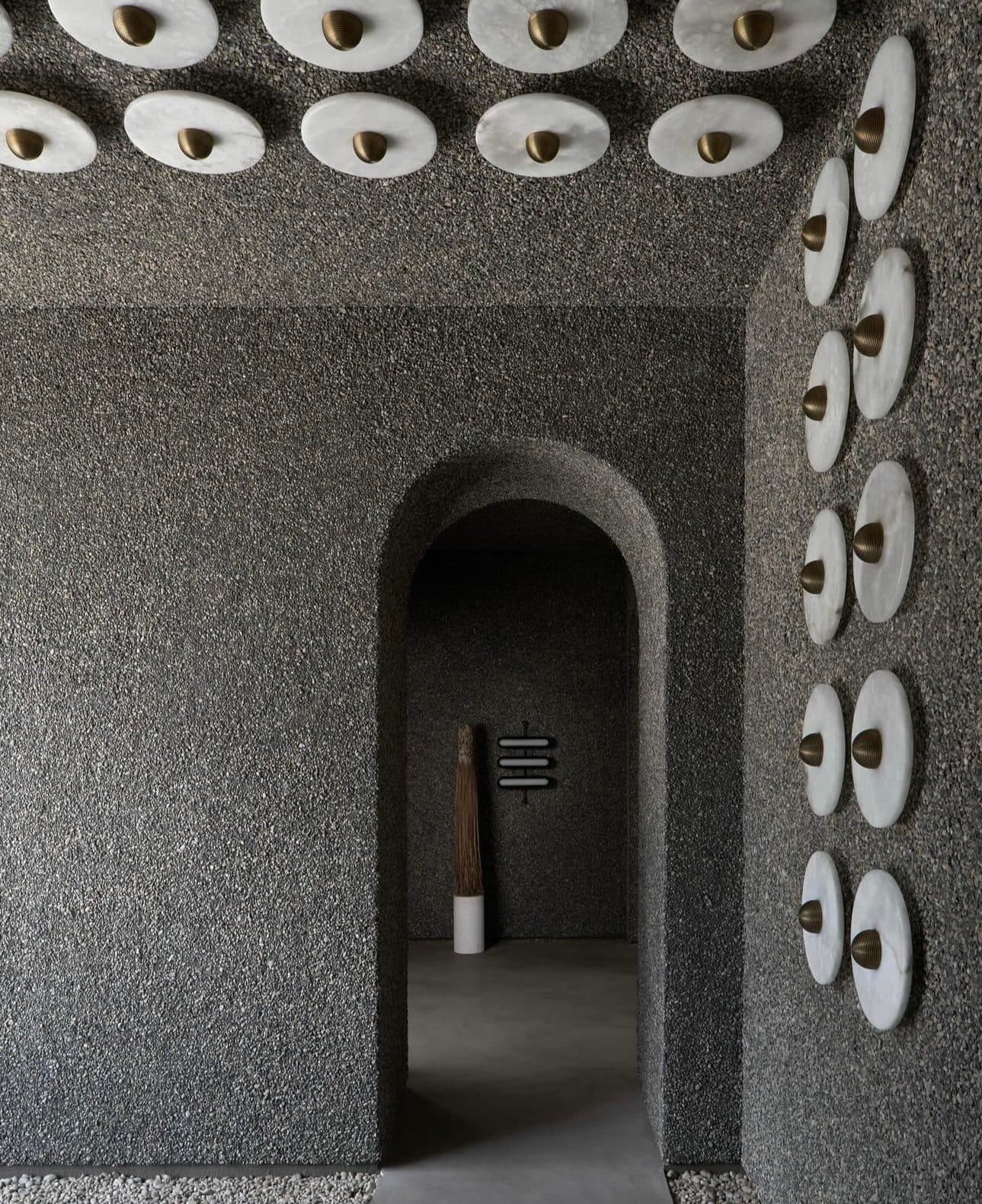 An arched doorway and walls in deeply pitted Meoded Vega plaster, with round alabaster sconces